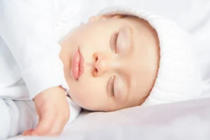 Bebis 5 månader som sover på rygg i vit mössa