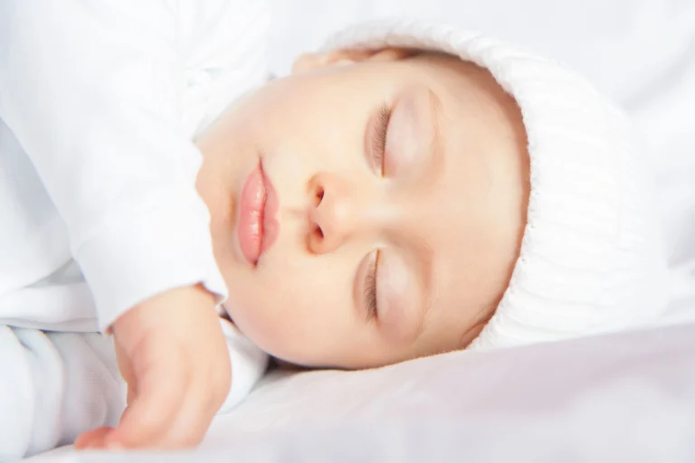 Bebis 5 månader som sover på rygg i vit mössa